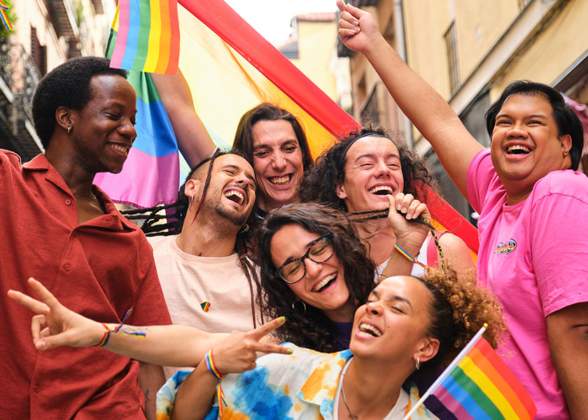 A group of people outdoors, having fun and laughing with LGBTQ+ rainbow flags.